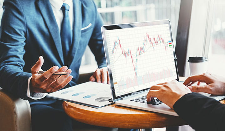 Dos propietarios de negocios revisando los datos y gráficos de inversión de BOK Financial en una laptop.